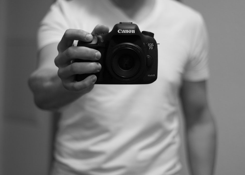 grayscale photo of man holding Canon camera