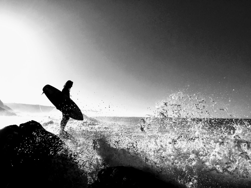 grayscale photography of man carrying surfboard on body of water