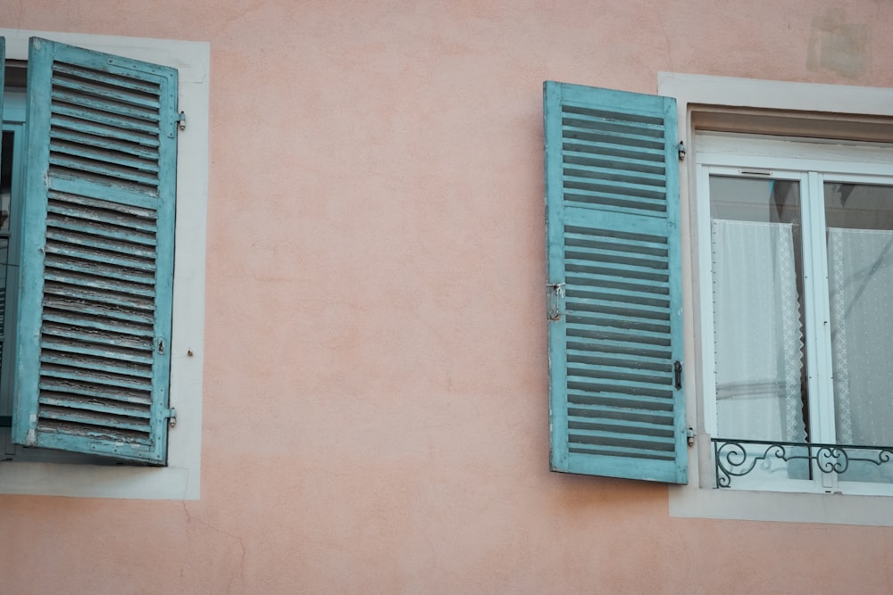 two windows with blue shutters on a pink wall