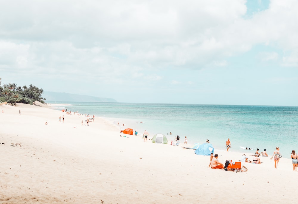 people walking and others are sunbathing on beach under white and blue sky