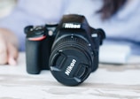 Nikon DSLR camera displayed with a zoom lens against a soft blurred background.