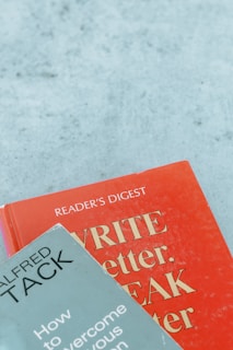 Two books are arranged on a surface, with one book titled 'WRITE Better, SPEAK Better' in red and the other titled 'How to Overcome Your Nervous Tension' by Alfred Tack in a muted green color.