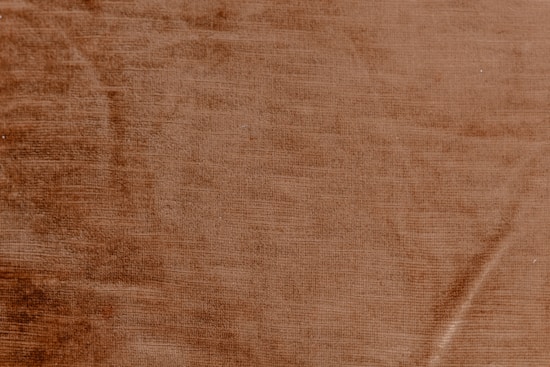 A textured surface with a warm, earthy tone resembling a close-up of a fabric or a material with subtle linear patterns.