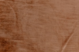 A textured surface with a warm, earthy tone resembling a close-up of a fabric or a material with subtle linear patterns.