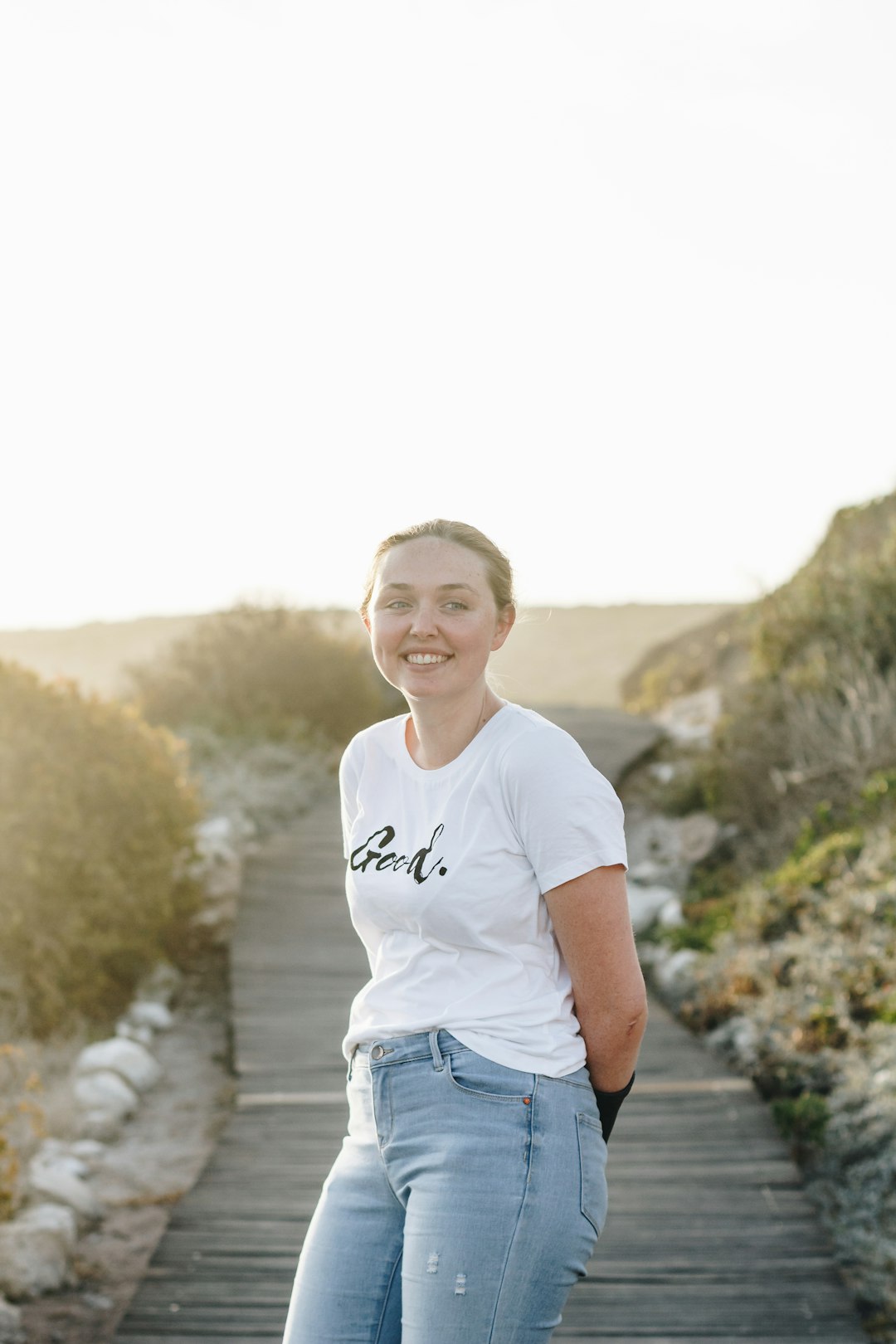 woman wearing white and black printed crew-neck t-shirt standing on wooden pathway smiling