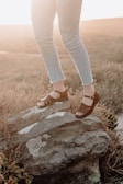 person wearing blue denim jeans and brown hiking sandals standing on gray rock