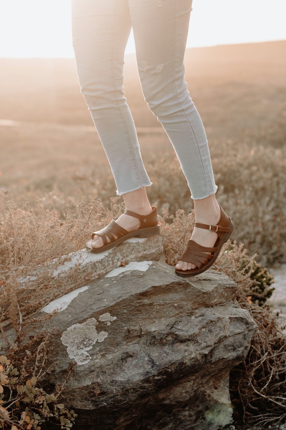 person wearing blue denim jeans and brown hiking sandals standing on gray rock