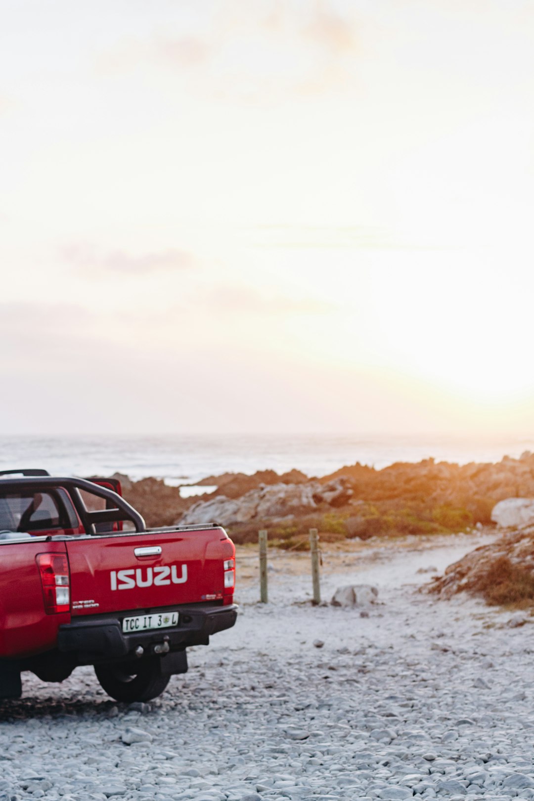 red Isuzu pickup truck parking near seashore under white sky