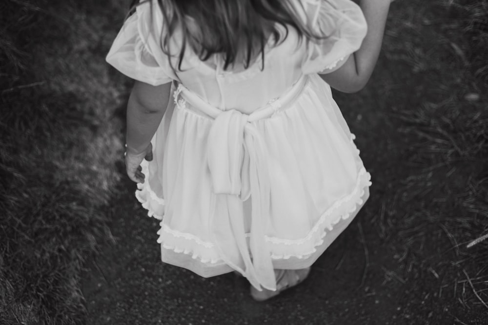 grayscale photography of child wearing dress standing while facing back