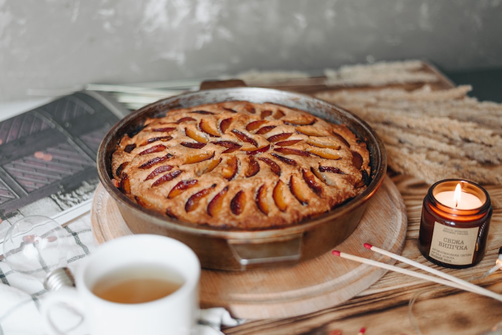 baked pie in round tray near lighted scented candle, light bulb, and white ceramic teacup