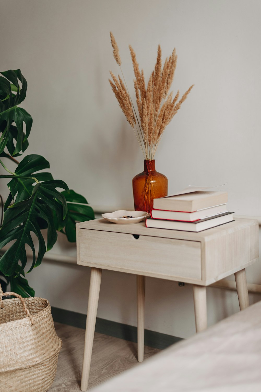 brown decorative wheat in brown ceramic vase near books on white wooden end table beside green leaf plant