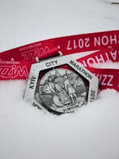 A silver medal with an intricate design featuring figures and the inscription 'KYW CITY MARATHON' and '21,0975 KM'. The medal rests on snow with a bright red ribbon that has text printed in white.