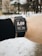 A person is wearing a smartwatch on their wrist, displaying a distance of 5.08 kilometers. The background is a snowy outdoor setting with some trees and buildings visible.