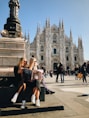 two women sitting on a bench in front of a cathedral