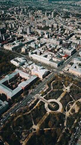 Aerial view of an urban landscape with densely packed buildings and streets forming a grid pattern. There is a large circular park area with trees and pathways situated prominently, surrounded by roads and vehicles.