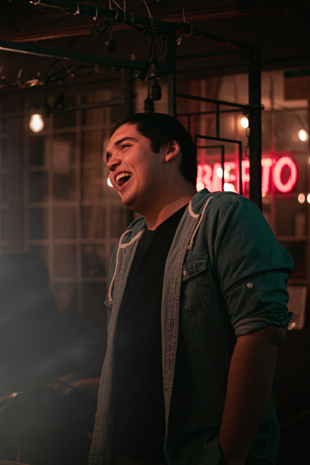 man wearing blue denim jacket standing and laughing during night time