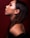 Profile view of a woman with smooth skin and long brown hair, featuring subtle makeup with reddish eyeshadow. She is wearing small hoop earrings and positioned against a deep red background.