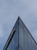 A sleek glass facade reflecting a cloudy London sky, framed by sharp concrete edges.