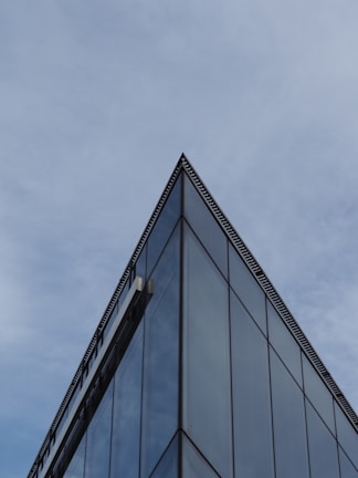 A sleek glass facade reflecting a cloudy London sky, framed by sharp concrete edges.