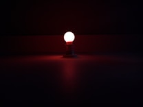 A small red light bulb is illuminated against a dark background, casting a gentle glow on the surface below.