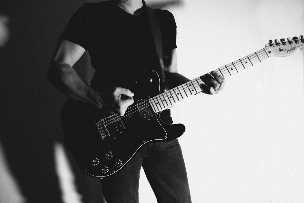 fotografia in scala di grigi di un uomo in piedi mentre suona la chitarra