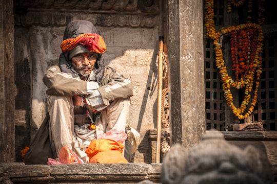 old man wearing gray and white jacket sitting outside building in Kathmandu Nepal
