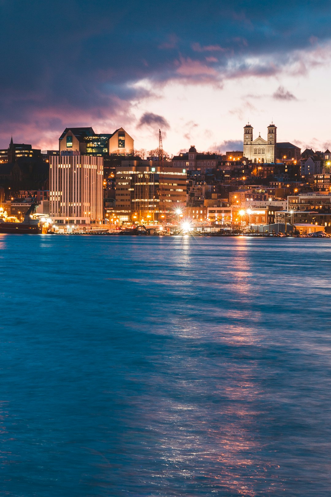 city with high-rise buildings near body of water under white and blue sky during night time