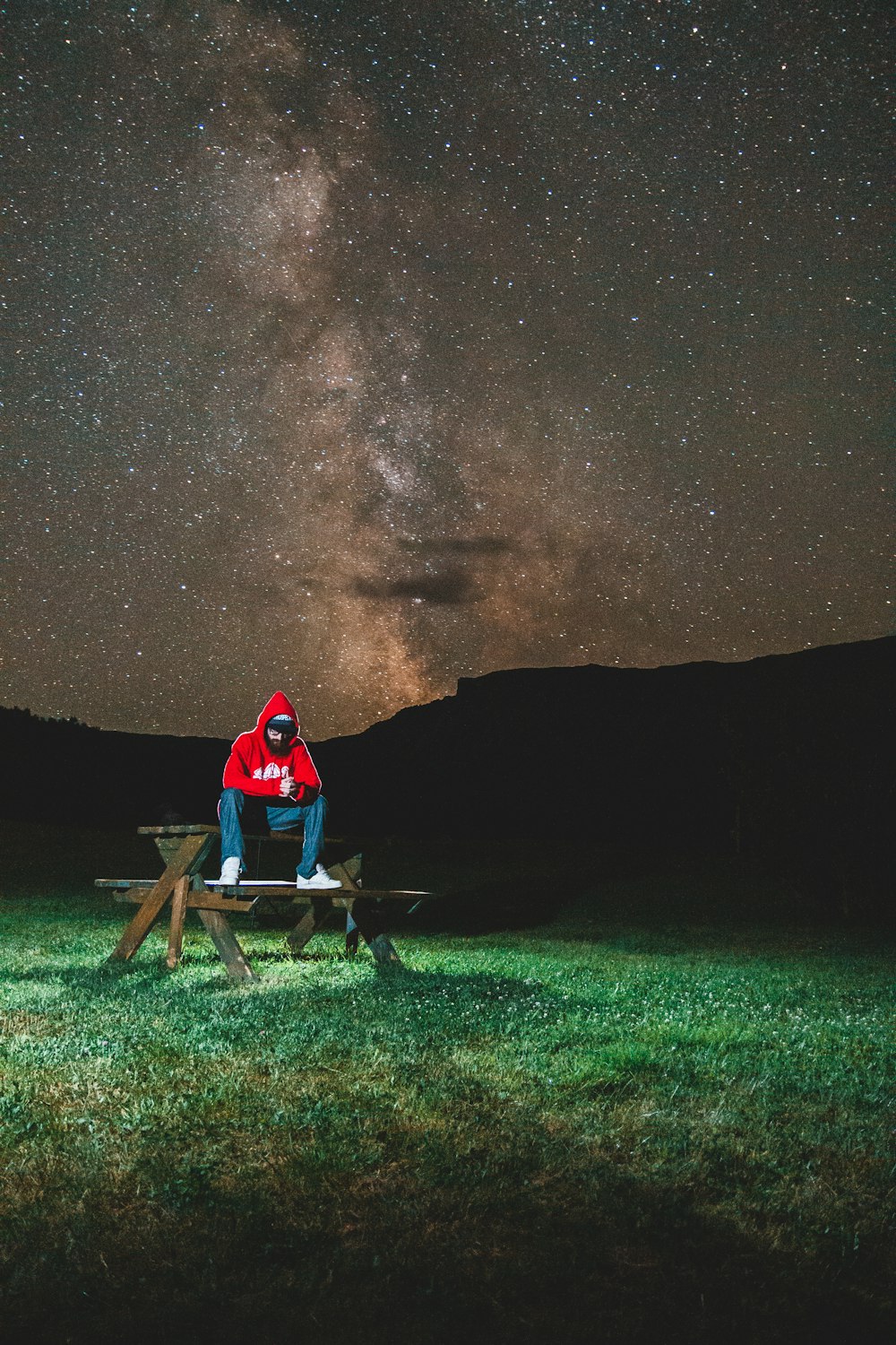 a man sitting on a bench under a night sky filled with stars