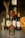 A selection of liquor bottles, including whiskey and wine. They are arranged neatly on a speckled gray surface alongside a jar of instant coffee and a wicker basket holding vibrant orange and yellow flowers. In the background, there are decorative wheat stalks in a holder.