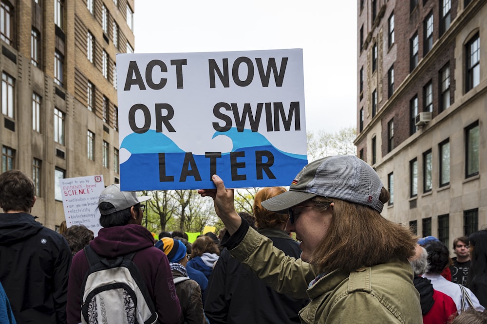 「Act now or swim later」の看板を掲げている女性