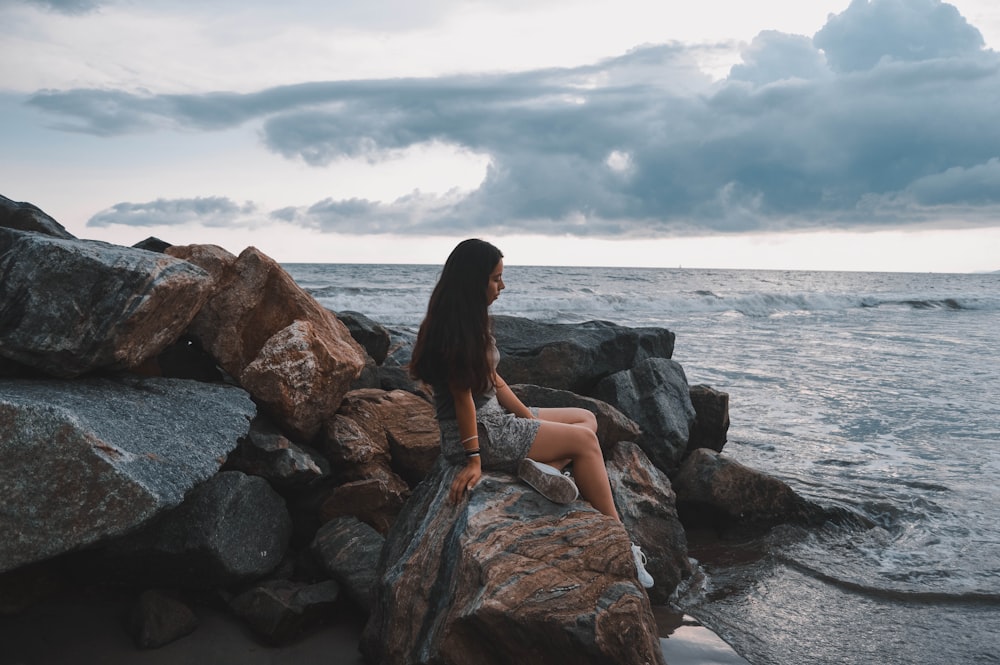 mulher sentada em rochas à beira-mar durante o dia