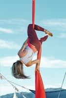 A performer mid-air on a trapeze, framed by a clear blue sky during a workshop session.