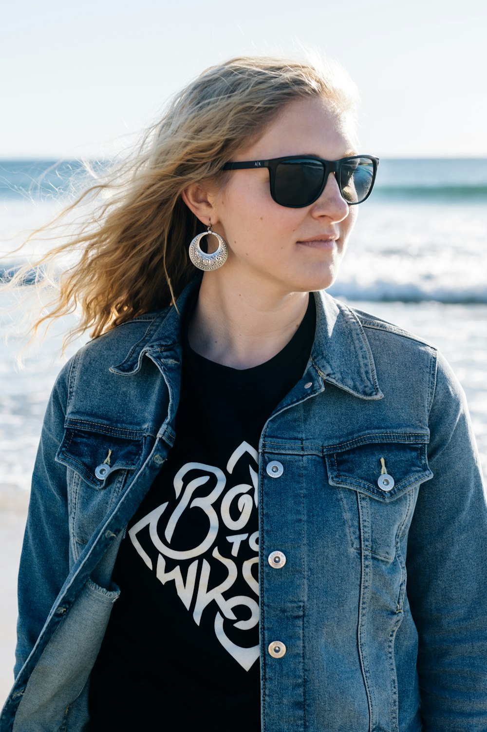 selective focus photography of woman wearing blue denim jacket standing on seashore