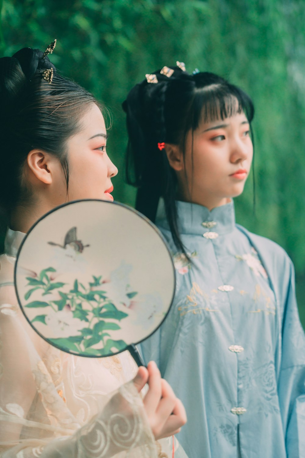 selective focus photography of two women wearing traditional dresses near green trees during daytime