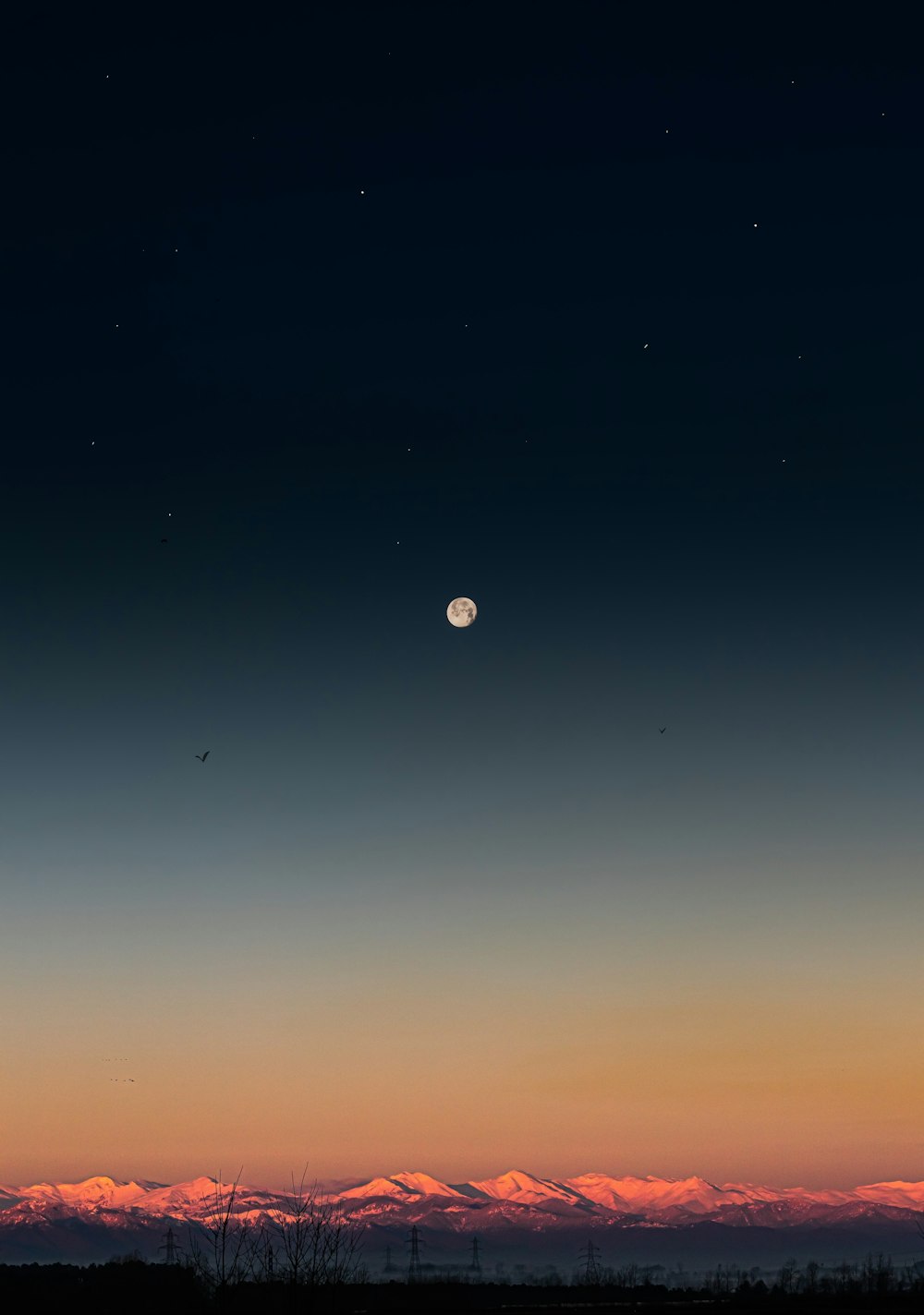 Una luna llena se ve en el cielo sobre una cordillera