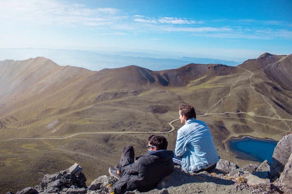 two men sitting on mountain during daytime