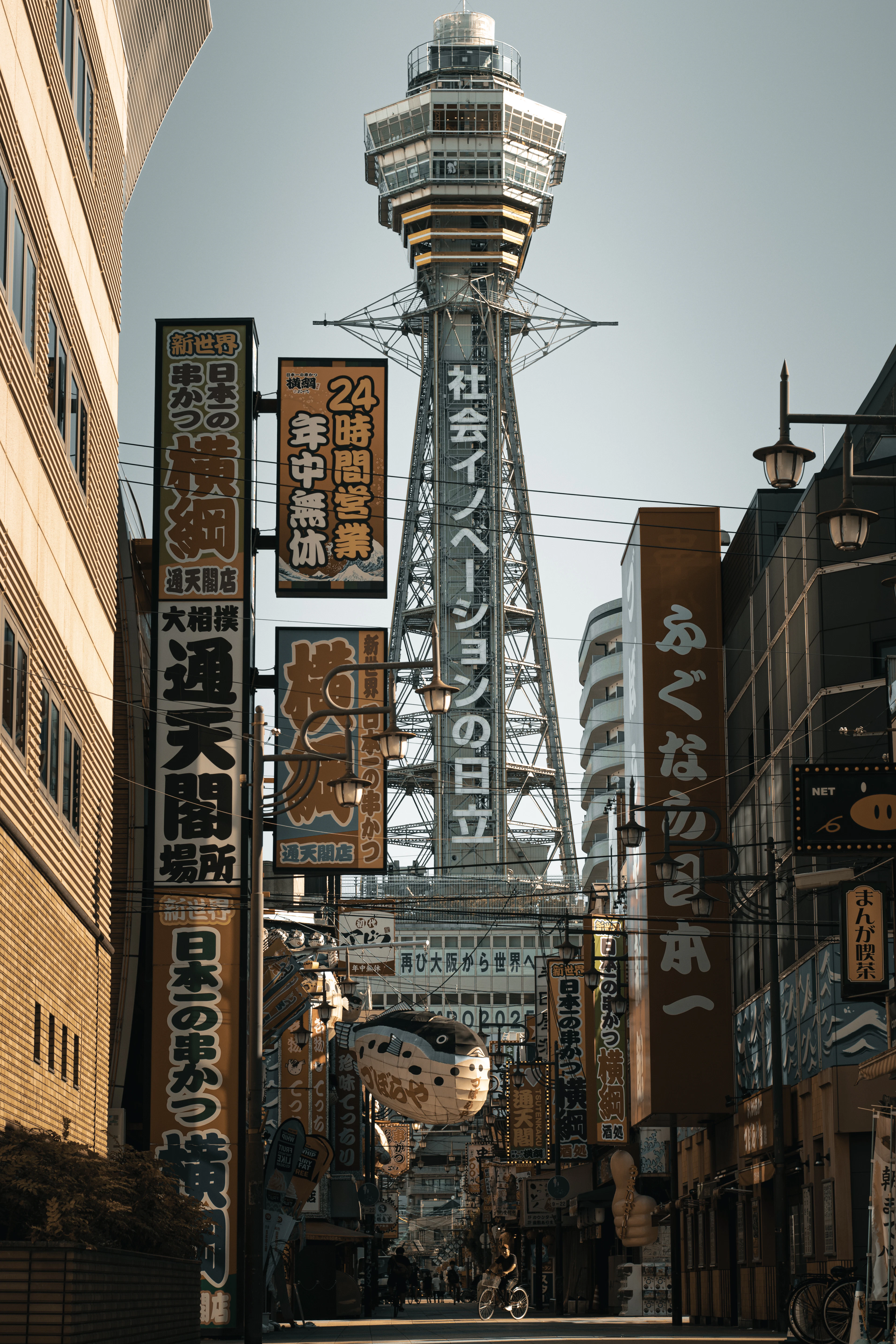 The Tsutenkaku Tower rises symmetrically above colorful shop signage on a Shinsekai street.
