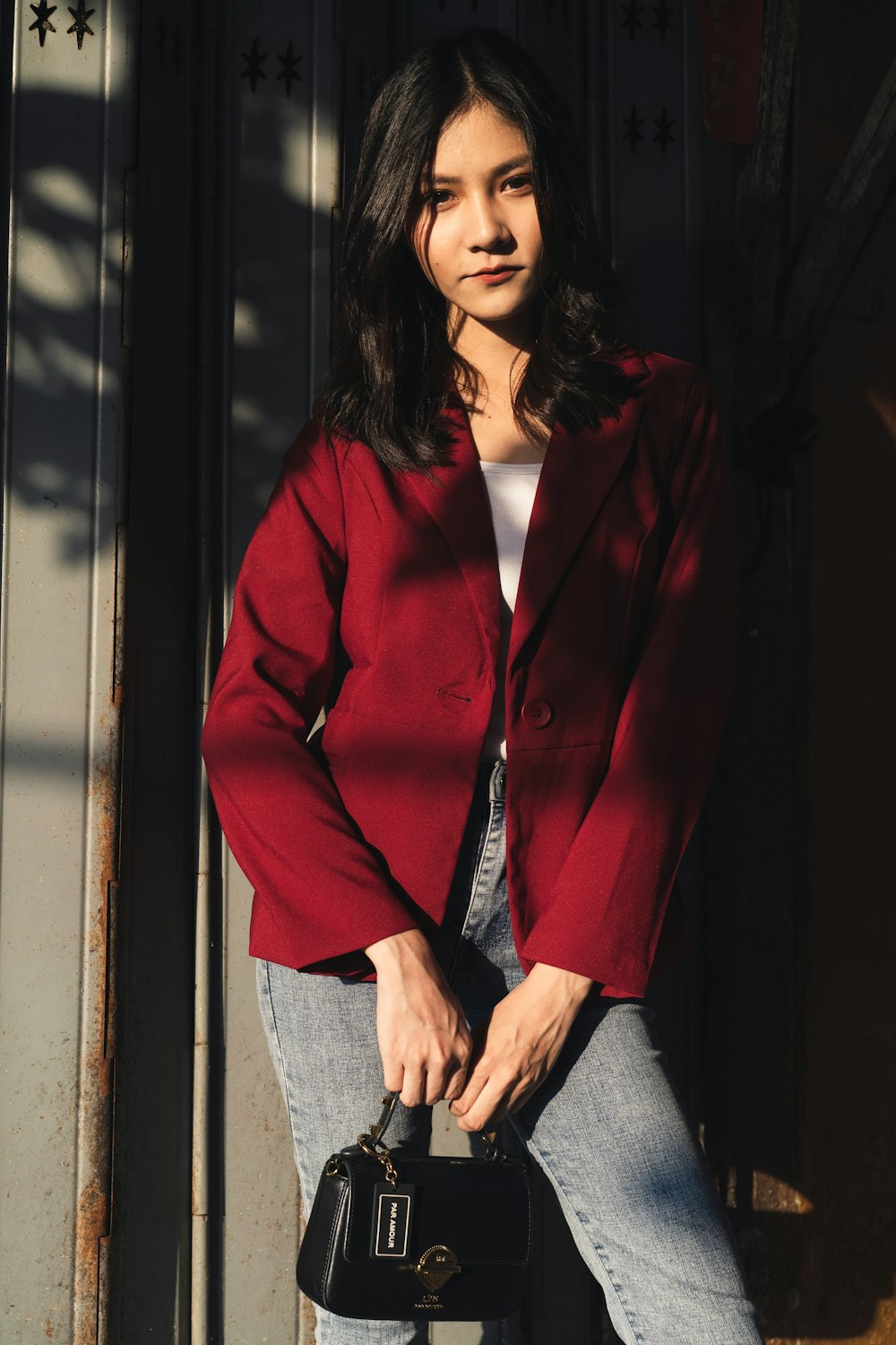 Foto de enfoque superficial de mujer con chaqueta roja sosteniendo un bolso de cuero negro