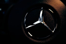 A close-up view of a metallic emblem on a textured black background, illuminated with subtle lighting that highlights its reflective surface.