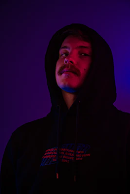 Moody shot of a black hoodie with a subtle metallic band logo glowing under purple neon.
