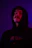 A close-up photo of a fan wearing a deep purple Ishaan hoodie under moody neon lighting.