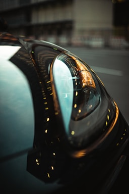 A close-up shot of a sleek car headlight reflecting city lights at dusk.