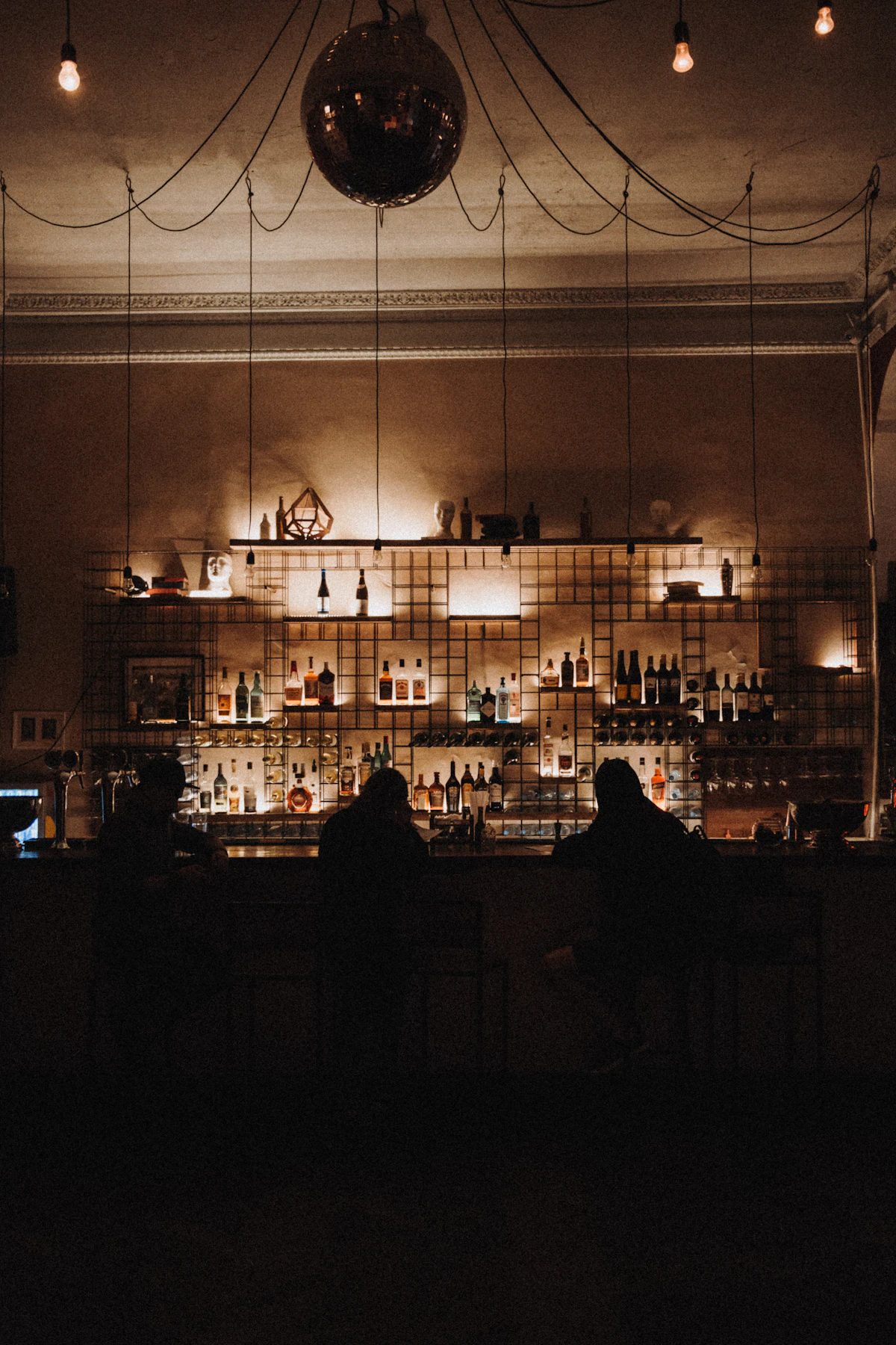Bottles and short glasses lined along a dark timber bar under a single warm lamp at Casa Lumbre.