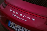 The rear view of a red Porsche 911 Carrera 4 with its logo and model name prominently displayed. The license plate shows registration from Germany and features EU markings.
