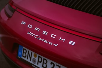 The rear view of a red Porsche 911 Carrera 4 with its logo and model name prominently displayed. The license plate shows registration from Germany and features EU markings.