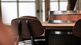 A wooden table is surrounded by dark wooden chairs. In the background, there is a wooden bucket with metal rings. The setting appears to be indoors, possibly at a restaurant or a café, with large windows that allow some light to filter in.