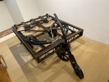 A wooden mechanical device with interlocking gears and pulleys, likely an early machine or model. The structure is set on a wooden surface and appears to be an engineering construct, possibly a historical or replication piece demonstrating mechanics.