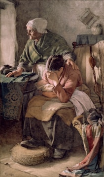 An elderly woman with a shawl comforts a younger woman who is seated and appears distressed, covering her face with her arm. The scene is set in a modest, dimly lit room with simple furnishings and textiles.