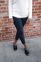 A model wearing a sharp, comfortable knit sweater paired with classic chinos, standing against a brick wall.