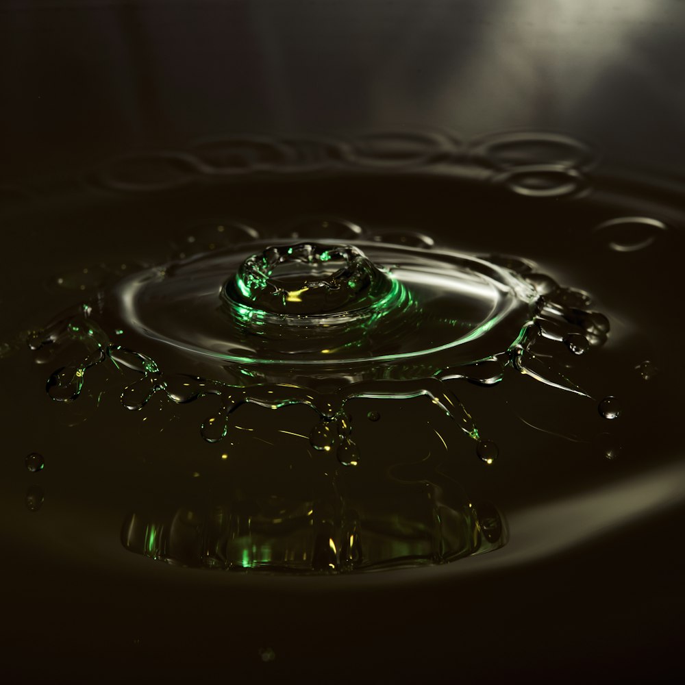 a water drop with a green light reflecting off of it